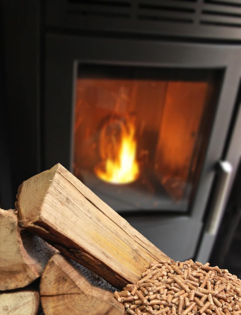 Bûches et granulés de bois : Le plein d'énergie pour votre poêle Bûches et granulés de bois empilés, avec un poêle à bois noir et ses flammes ardentes en arrière-plan.